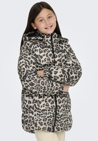 Pārklāta leopardu raksta jaka bēšā un melnā krāsā ar kapuci, ar rāvējslēdzēju, elastīgām piedurknēm un brīvu piegriezumu, kas paredzēta siltumam un komfortam.