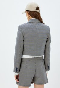 Geruit blazer gemaakt van textuurstof met een cropped ontwerp, gecombineerd met bijpassende hoge shorts. Voorzien van blauwe accenten en knopen.