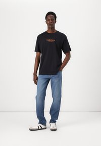 Sort bomulds T-shirt med orange "Creative Works" tekst, parret med blå denim jeans og beige sneakers med sorte striber.