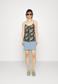 Camisola preta floral com alças finas, combinada com uma saia mini de ganga azul clara. O modelo usa sandálias plataforma verdes e óculos de sol rosa oversized.