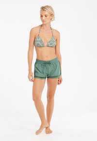 Bikini vrch s geometrickým vzorom v zelených a žltých odtieňoch, doplnený jednofarebnými zelenými kraťasmi so šnúrkami na stiahnutie. Hladká textúra, priliehavý strih a dĺžka po stred stehien.