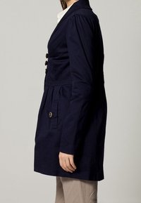 Laivastonsininen puuvillapikkutakki, jossa istuva siluetti, napitukset ja sivutaskut. Takissa on puffihihat ja laskostettu selkäosa.