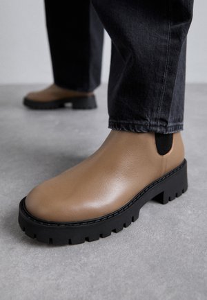 Bocanci din piele maro, cu talpă groasă neagră și panouri laterale elastice. Textură netedă cu un design al degetului rotunjit.