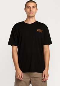 Sort kortærmet t-shirt lavet af bomuld, med et orange Volcom-logo på venstre bryst. Rund halsudskæring og afslappet pasform.