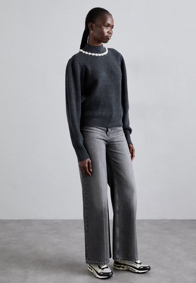 Sweat-shirt en tricot côtelé gris foncé avec un col montant, rehaussé d'un col de couleur claire, associé à un jean gris à jambes larges et des baskets noires.