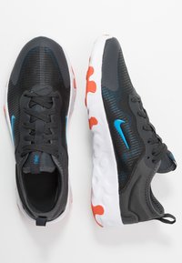 Chaussures de sport noires avec des accents bleus, tige en maille texturée et semelle intermédiaire blanche avec des détails orange. Design à lacets avec une languette à l'arrière.