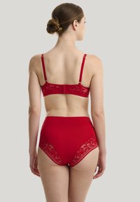 Rotes Spitzen-Bralette und hochgeschnittene Unterwäsche. Das Bralette verfügt über verstellbare Träger und einen Hakenverschluss; die Unterwäsche hat Spitzenakzente an den Seiten.
