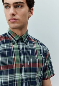Kurzarm-Hemd aus Karomuster in Navy, Gr�ün, Rot und Weiß; mit Button-Down-Kragen; und kleinem Markenpatch auf der Brusttasche.