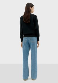 Zwarte trui met een geribbelde onderkant en mouwen, gecombineerd met lichtblauwe, wijde jeans met achterzakken. Soepele texturen en een casual pasvorm.