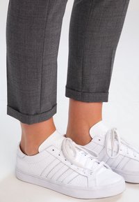 Pantaloni grigi a sigaretta con orli arrotolati abbinati a sneaker bianche testurizzate con tre strisce laterali e chiusura con lacci.