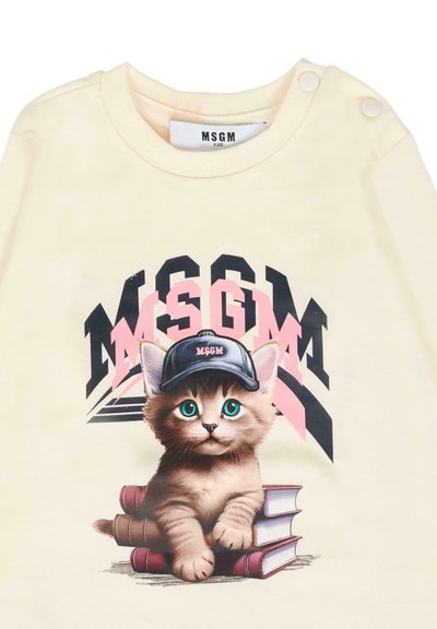 Kitten met blauwe ogen die een zwarte MSGM-pet draagt, liggend op gestapelde boeken met het MSGM-logo in zwart en roze erachter op crèmekleurige stof.