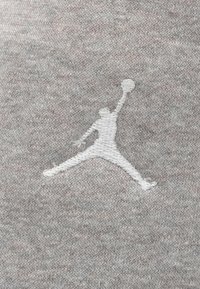 Λευκό κεντημένο περίγραμμα ενός παίκτη μπάσκετ που πηδάει με μια μπάλα σε γκρι πλεκτό ύφασμα.