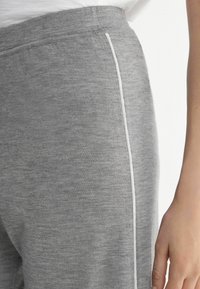 Grå sweatsbyxor med en slät textur, som har en smal vit sidrand och ett elastiskt midjeband synligt längs den övre kanten.