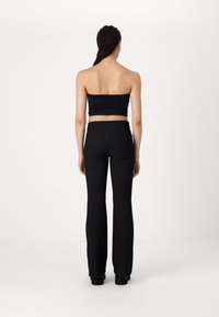 Zwart strapless top met geplooide textuur en hoge taille, wijde zwarte broek. Glad materiaal, minimalistisch ontwerp, geen zichtbare hardware.