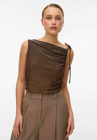 Bronzinė be rankovių palaidinė su drapiruotu dizainu, tekstūruotu paviršiumi ir šoniniu surišimu. derinamas su šviesiai rudiems pritaikytais kelnėmis.
