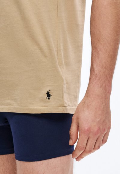 Μπεζ βαμβακερό T-shirt με διακριτική υφή, διακοσμημένο με μαύρο κεντημένο λογότυπο στο τελείωμα, συνδυασμένο με σορτς σε ναυτικό μπλε χρώμα.