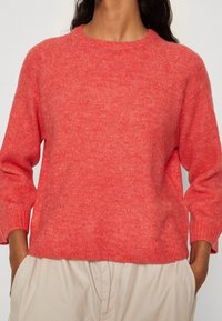 Korallinpunainen neulepaita pyöreällä pääntiellä, resorihihansuiden ja rento istuvuus. Pehmeä pinta ja keskiverto painoinen kangas.