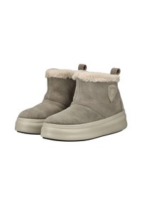 Ein Paar beigefarbene Wildleder-Ankle-Boots mit dicker weißer Kunstfellumrandung und Gummisohlen, ausgestattet mit einem seitlichen Logo-Patch und Zuglaschen an der Rückseite.