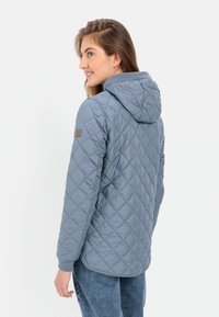 Gequilted capuchonjack in lichtblauw, met een gestructureerd oppervlak, lange mouwen en een logopatch op de linker schouder.