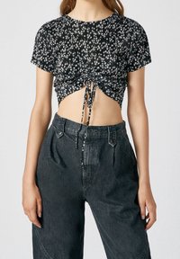 Haut court noir à motif floral avec manches courtes et détail froncé à l'avant ; associé à un pantalon taille haute gris foncé texturé.