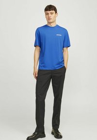 Mėlyna trumpomis rankovėmis marškinėliai su apvaliu kaklu, pagaminti iš lygaus audinio. Sugretinti su juodomis siaurėjančiomis kelnėmis ir juodais raištiniais bateliais.