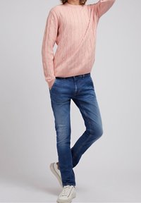 Hellrosa Kabelstrickpullover mit rundem Halsausschnitt, kombiniert mit blauen Slim-Fit-Jeans und weißen Sneakers. Lässiges Design, geeignet für den täglichen Gebrauch.