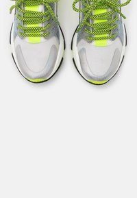 Zapatillas deportivas con parte superior de malla en gris y detalles en amarillo neón, suelas negras y cordones texturizados. Detalles reflectantes en los laterales.