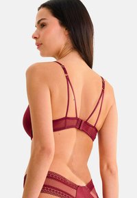 Soutien-gorge bordeaux avec des détails en maille transparente, des bretelles réglables et une fermeture au dos. Présente une finition en dentelle festonnée le long de la bande.