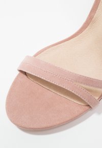 Gros plan d'une sandale à bout ouvert en daim rose avec une bride unique sur les orteils et une semelle intérieure beige texturée.