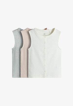 Junges Mädchen mit lockigem Haar schaut nach unten, während sie einen rosa Pullover hält. Sie trägt ein graues, geknöpftes Oberteil, weite Jeans und beige Schuhe.