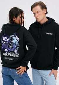 Kaks modelligi kannavad musta kapuutsiga sviitrit, millel on tekst "Memorize"; ühelt näeb seljal lilla koi kalaga ja lillemustriga disaini, teine on näoga kasutaja poole.