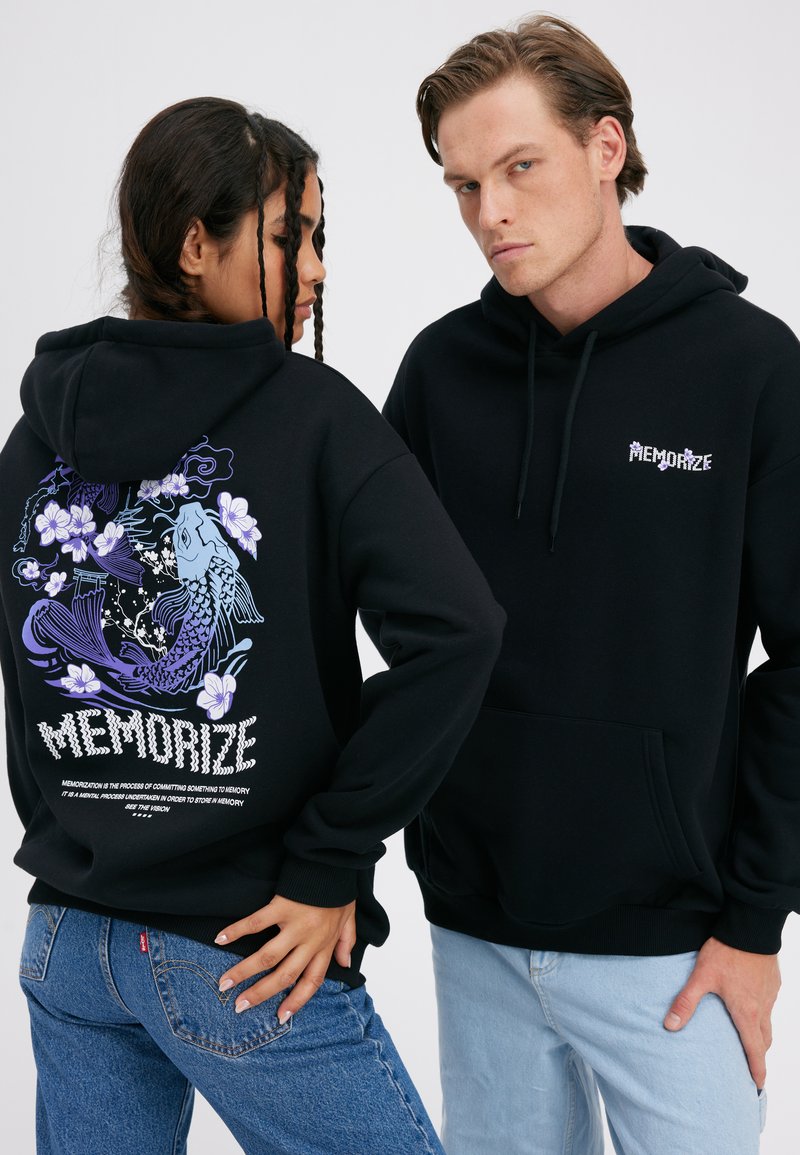 Kaks modelligi kannavad musta kapuutsiga sviitrit, millel on tekst "Memorize"; ühelt näeb seljal lilla koi kalaga ja lillemustriga disaini, teine on näoga kasutaja poole.