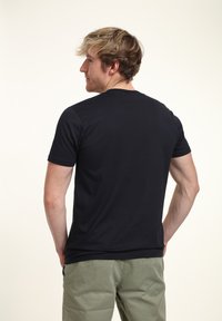 Černé tričko s krátkým rukávem a kulatým výstřihem, vyrobené z měkkého materiálu, s přiléhavým střihem a minimalistickým designem. Nosené s khaki kalhotami.