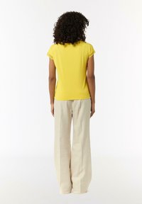 Yellow short-sleeve top with lace accents, paired with beige wide-leg trousers. Smooth texture with a relaxed fit, viewed from the back.