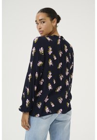 Navy blouse with long sleeves, featuring a floral pattern in pink and green. Soft texture, ruffled neckline, and loose fit.