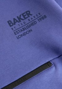 Lilla dress, millel on must reljeefne logo, millel on kiri "BAKER by TED BAKER ESTABLISHED 1988 LONDON." Pehme materjal ja sile tekstuur.