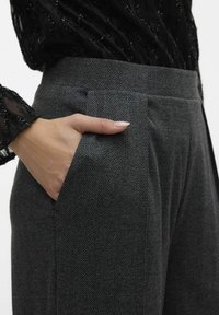 Pantaloni grigi a fantasia houndstooth con vestibilità sartoriale, dotati di tasche laterali e vita piatta, abbinati a un top nero textured.