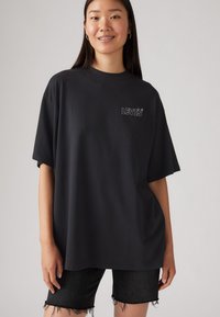 T-shirt noir oversize en coton doux, avec un petit logo gris LEVI'S sur la poitrine gauche. Assorti avec un short en denim noir usé.
