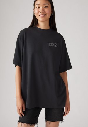 Crna oversized majica od mekog pamuka, s malim sivim LEVI'S logom na lijevoj strani grudnog koša. Uparena s istrošenim crnim trapericama.