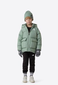 Mintgrøn vatteret jakke med hætte, sorte bukser, grå handsker og hvide sneakers. Jakken har lynlåslukning og forlommer.