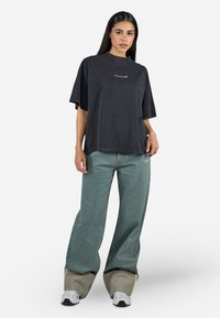 T-shirt en coton noir surdimensionné avec un col rond et un logo sur le devant. Associé à un jean bleu clair à jambes larges et des baskets grises imposantes.