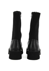 Para czarnych botków do połowy łydki z grubymi obcasami i tylnym zamkiem błyskawicznym, wykonanych ze skóry i tkaniny, pokazanych od tyłu na białym tle.