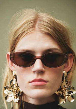 Sunglasses with dark lenses and narrow frames, paired with large, gold metallic flower earrings. Smooth texture and shiny finish.