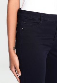 Námořnické džíny z denimu s pěti kapsami, hladkou texturou a přiléhavým střihem. Obsahují kontrastní švy a kovový detail na knoflíku v pase.