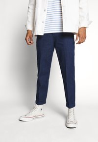 Vetsit tummansinisiä kapenevia farkkuja, yhdistettynä valkoiseen farkkutakkiin ja siniraidoitettuun t-paitaan sekä valkoisiin korkeatennareihin.