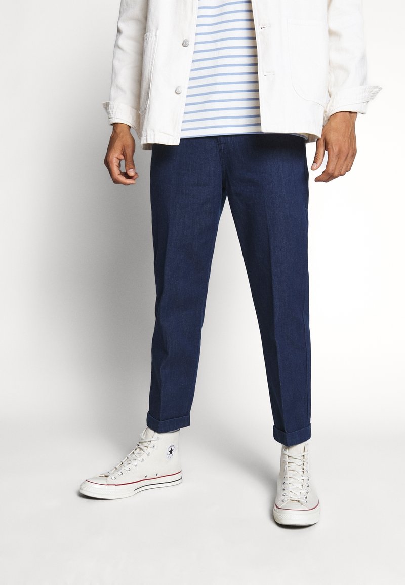 Vetsit tummansinisiä kapenevia farkkuja, yhdistettynä valkoiseen farkkutakkiin ja siniraidoitettuun t-paitaan sekä valkoisiin korkeatennareihin.