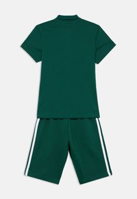 Zelené bavlnené polo tričko s krátkymi rukávmi a zodpovedajúce šortky. Šortky majú biele bočné pruhy. Hladká textúra, ležérny dizajn.