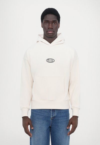Krämfärgad hoodies med dragkedja och en framficka samt en liten svart logotyp. Matchas med blå jeans som har en avslappnad passform och mjuk textur.
