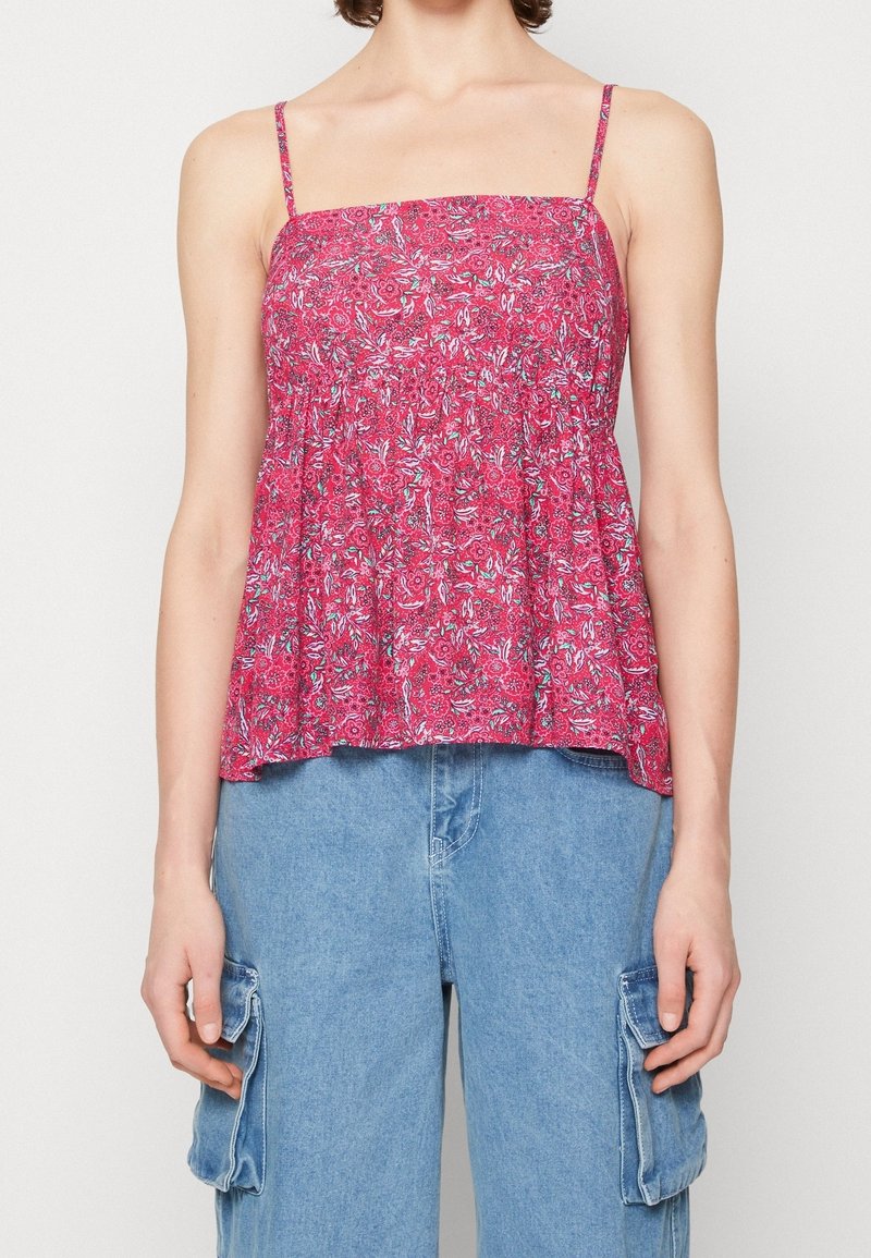 Haut sans manches rose à motif floral avec fines bretelles, associé à un pantalon cargo en denim bleu clair avec poches latérales.