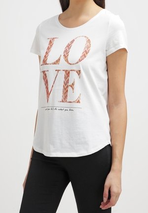 Witte T-shirt met korte mouwen met grote patroonletters die LOVE spellen en kleinere tekst eronder, gedragen met een zwarte broek.